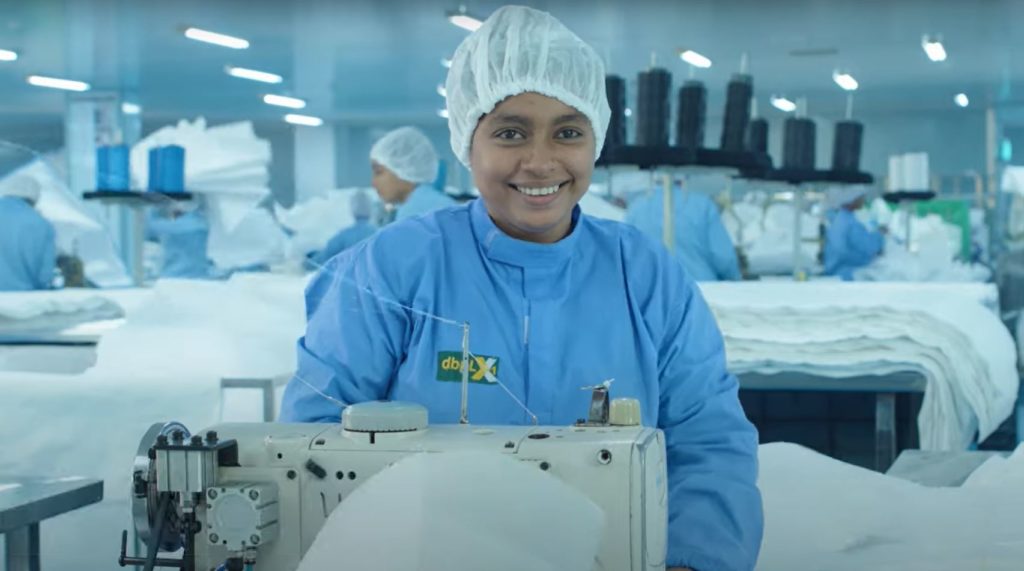 photo of woman in a factory smiling, wearing coveralls and a hairnet
