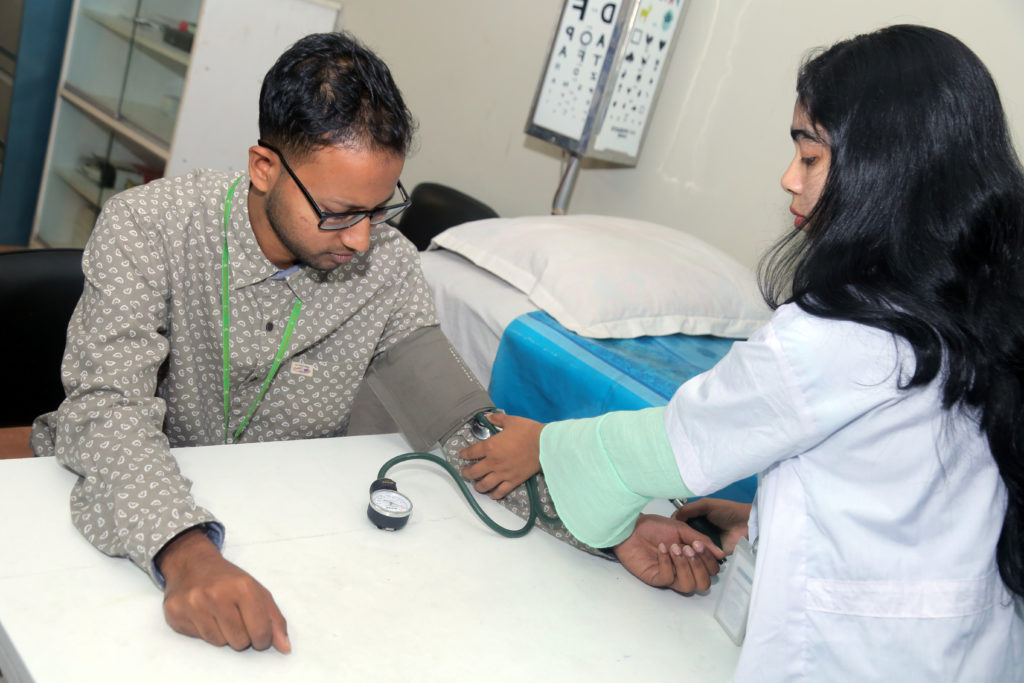 photo of person sitting at a table getting their blood pressure checked by anotehr person wearing a lab coat